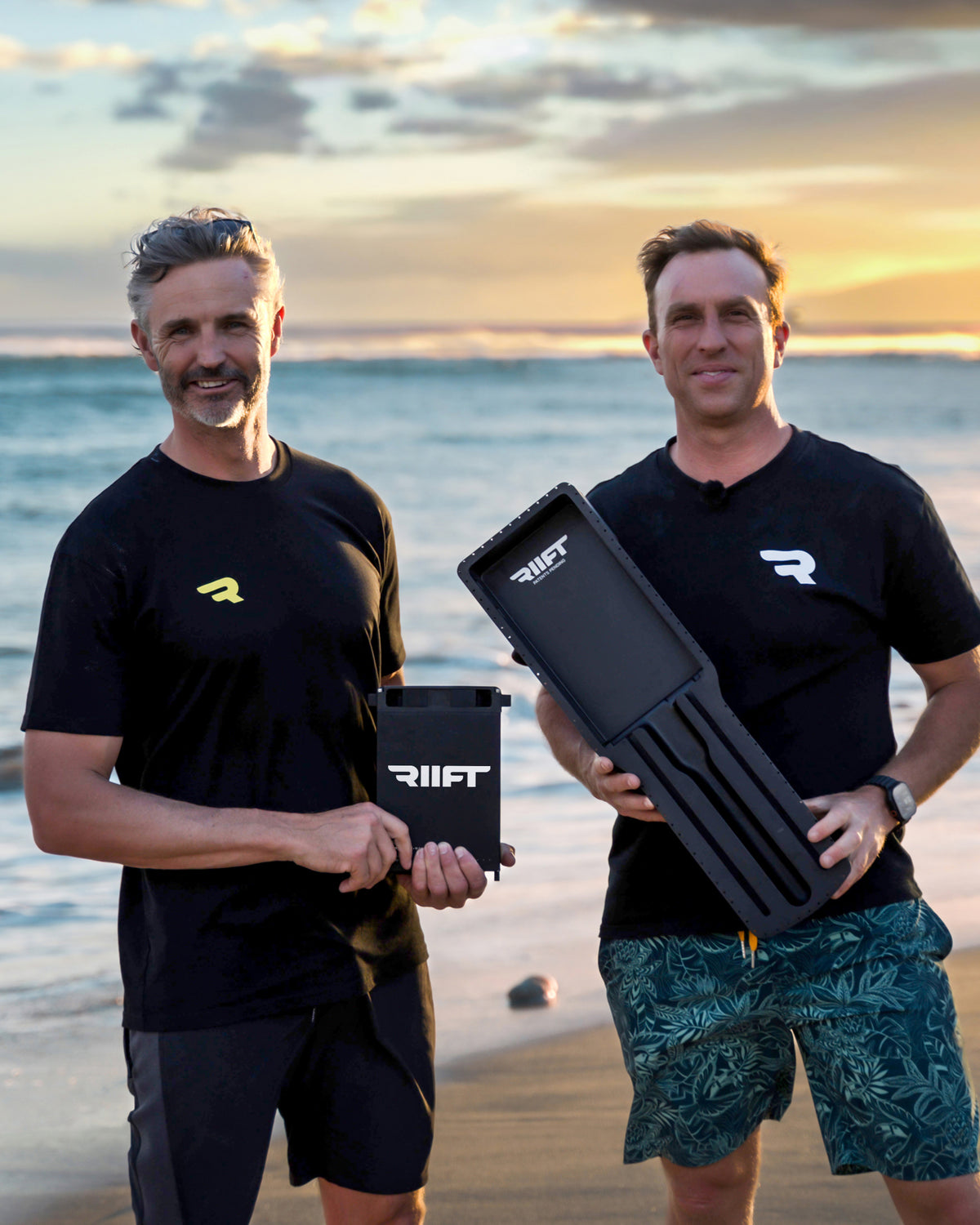 John and Al the founders of RIIFT, standing on a beach at sunset, each holding a RIIFT battery and RIIFT Tracks. 
