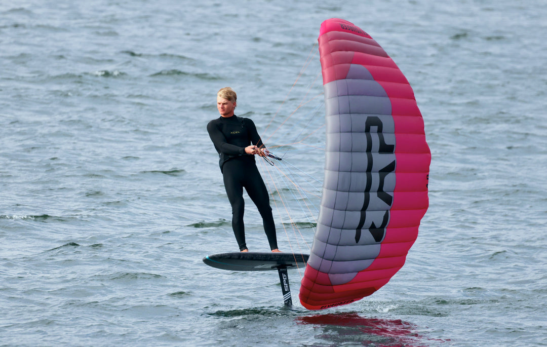 Nathan Van Vuuren parawing riding on a RIIFT-enabled board on open blue-green water while holding a large red, white, and blue parawing.