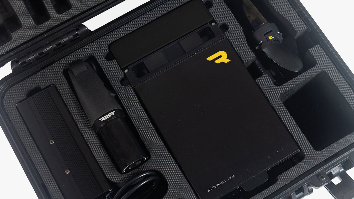 A black RIIFT PowerPack case showing the contents arranged in molded compartments. The most prominent item is a black RIIFT Battery Unit with large white 'RIIFT' branding on the front, alongside a parts of the RIIFT Propulsion Unit and other parts.