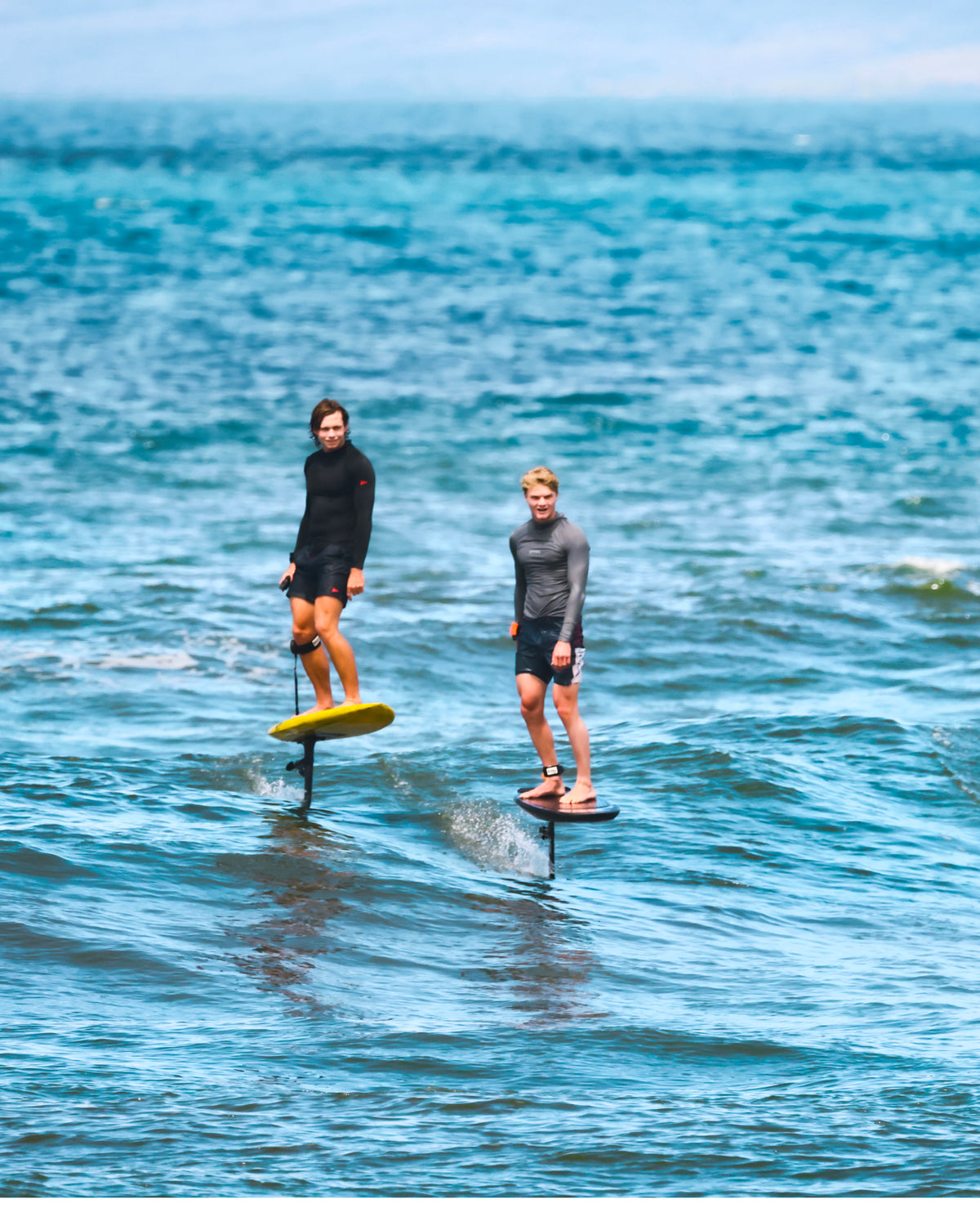 Kane De Wilde, Nathan Van Vuuren and Jarrod Snow standing on RIIFT-enabled boards in the ocean, wearing wetsuits and standing in turquoise water.