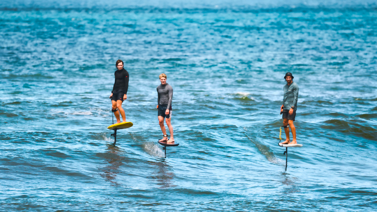 Kane De Wilde, Nathan Van Vuuren and Jarrod Snow standing on RIIFT-enabled boards in the ocean, wearing wetsuits and standing in turquoise water.